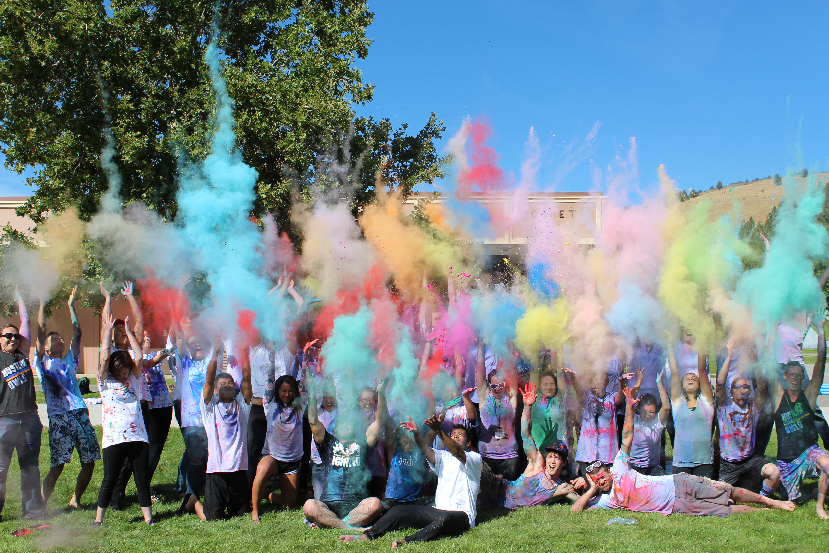 Students gathered on lawn throwing multi colored power in the air. 