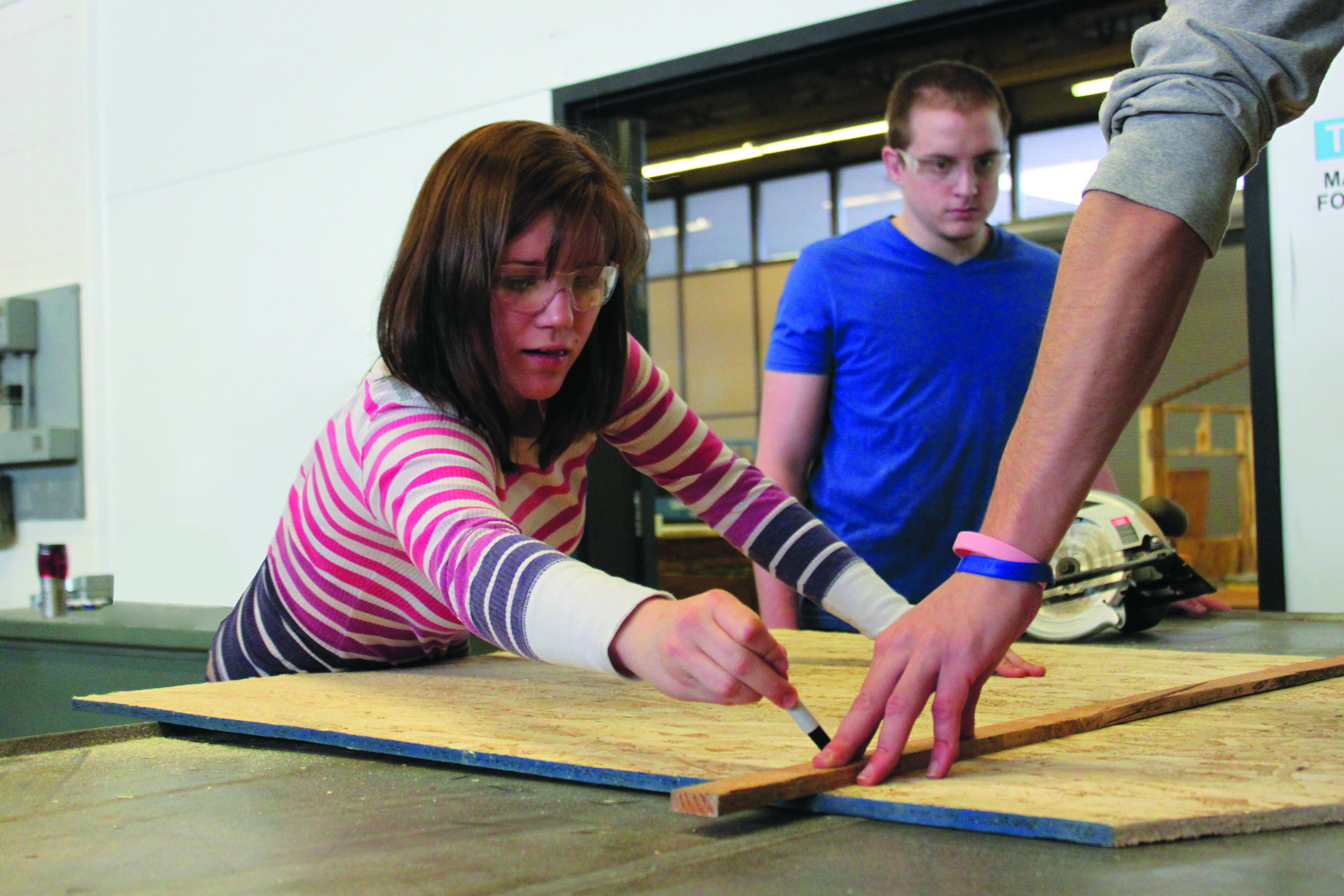 2 students work on measuring a piece of wood in an engineering lab