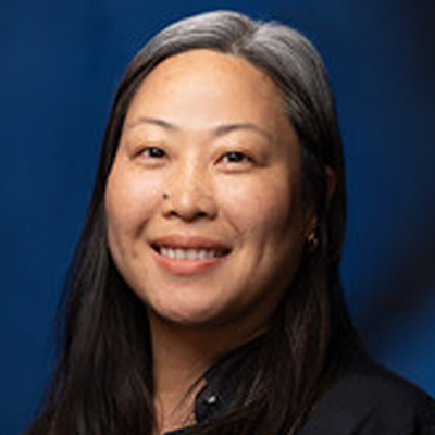 Portrait of Emy Martin with dark hair, dark shirt, with navy blue background