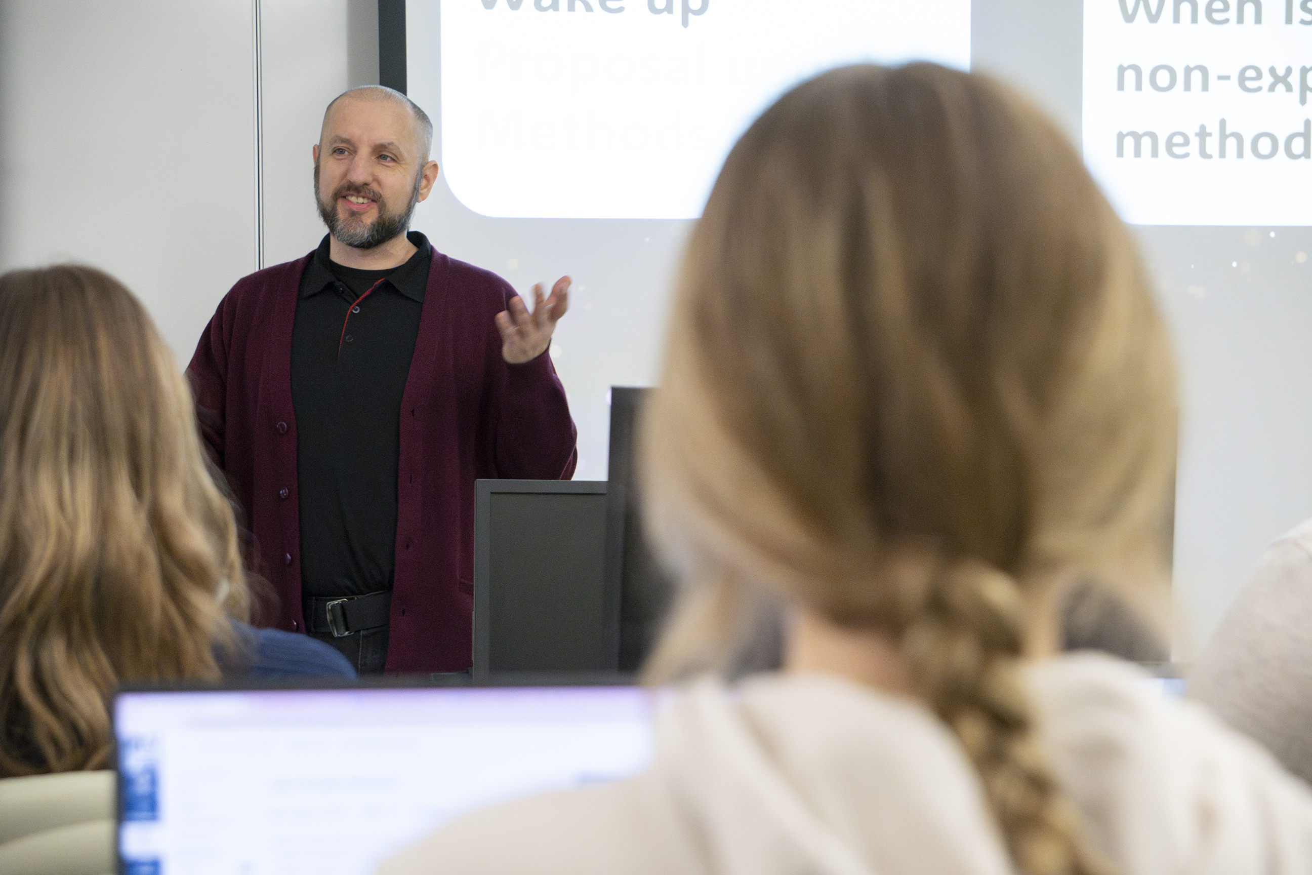 Professor stands in front of students engaged in conversation