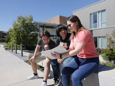 Students and counselor sitting on a low concrete wall talking, looking at information in a binder