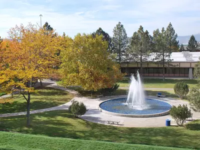 Picture of campus during fall. Includes grass, trees with fall foliage, and iconic Oregon Tech geothermal fountain