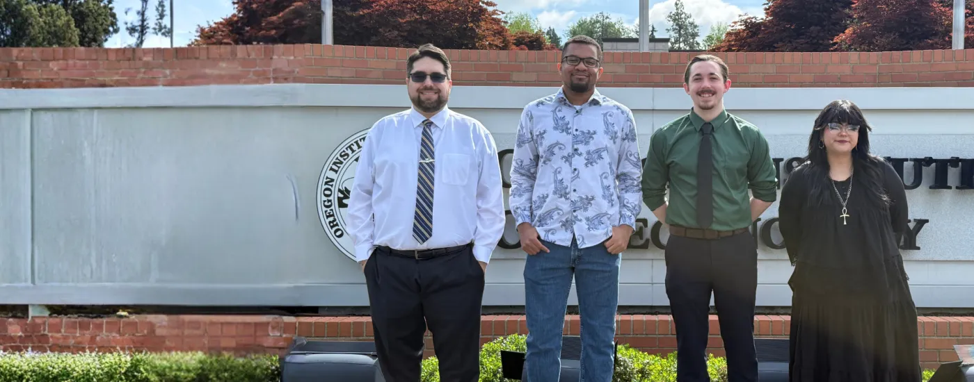 Four student government officers pose for a group photo in front of the Oregon Tech sign at the Portland-Metro campus. The U.S. flag, the Oregon flag, and Oregon Tech's flag are behind the sign.