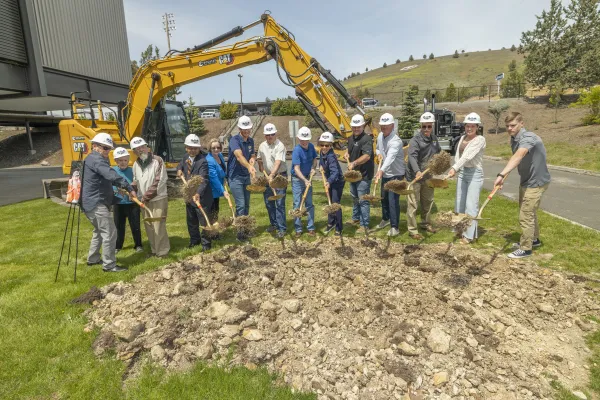 Group of people standing around dirt holding shovels and wearing hard hats